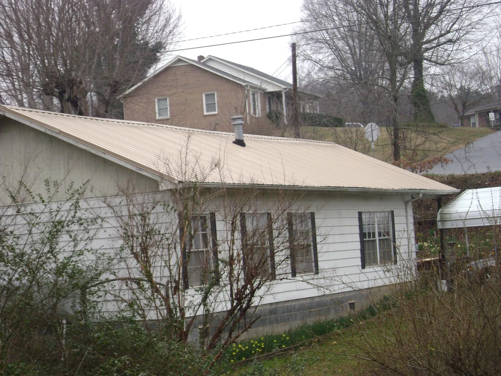 Tan metal roof on a white sided house set into a hillside — Commercial Roofing by Roofing Brothers in Virginia Beach